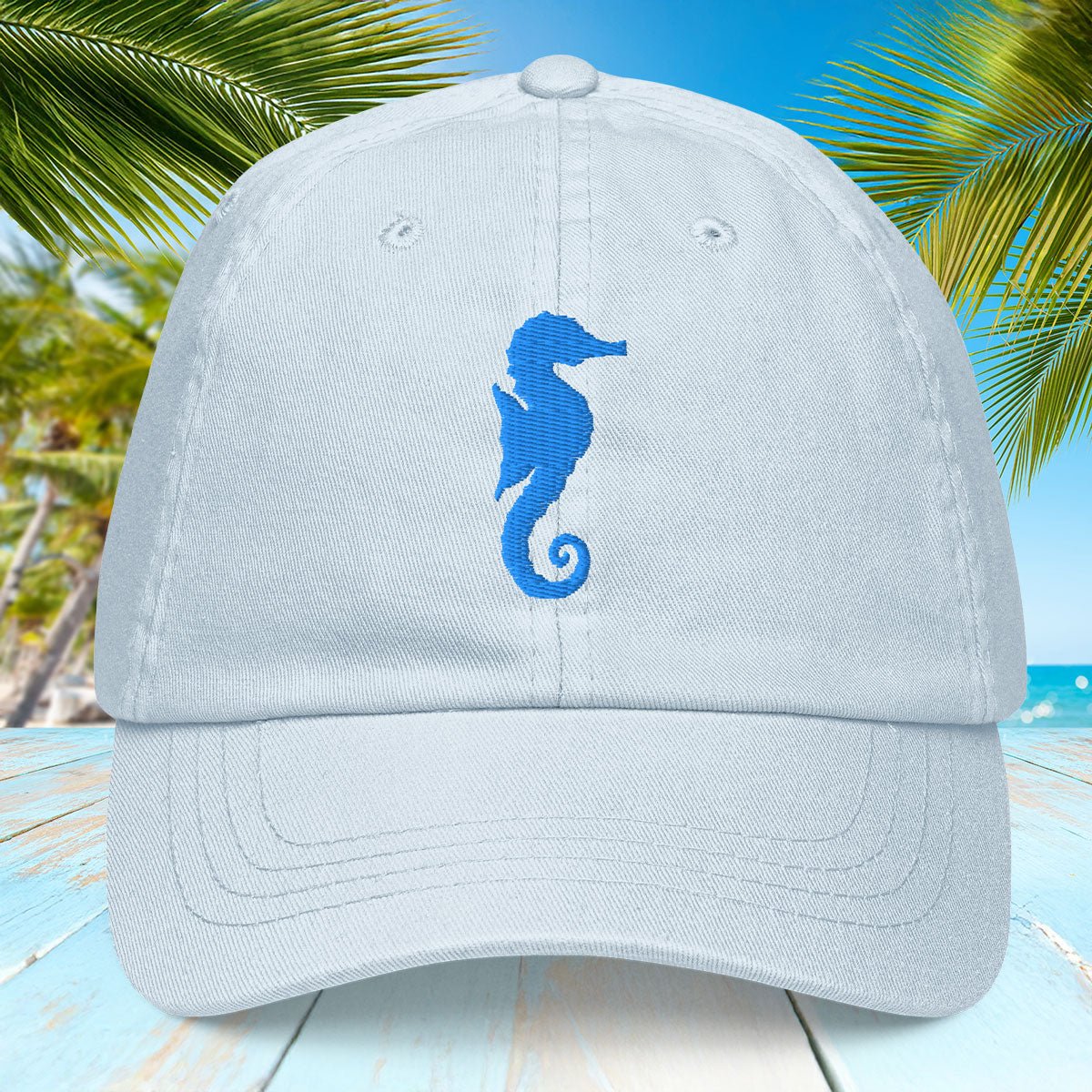 Pastel blue cap with blue embroidered seahorse design on a tropical background