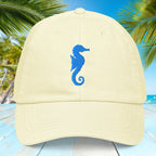 Pastel yellow cap with blue seahorse embroidery on a tropical background