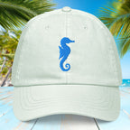 Light pastel mint green hat with blue embroidered seahorse design on a tropical background