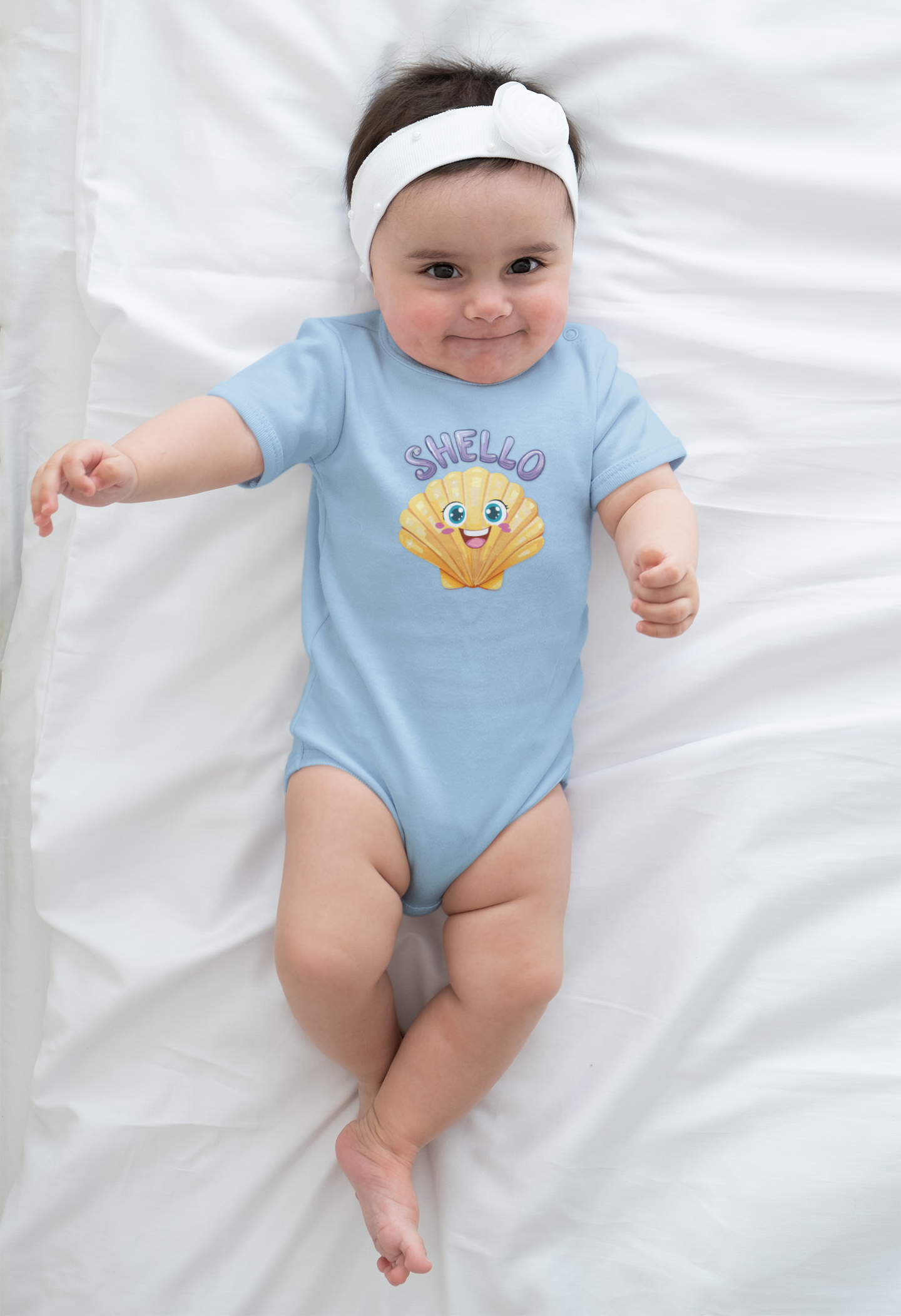 Baby wearing a blue onesie with a cartoon seashell character and Shello text, lying on a white blanket.