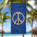 Beach towel featuring a dark blue sandy bottom sea floor adorned with seashells perfectly arranged to form a peace sign. The towel is hanging on a line outside a beach bungalow in Hawaii.