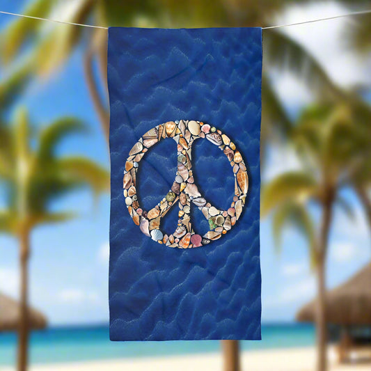 Beach towel featuring a dark blue sandy bottom sea floor adorned with seashells perfectly arranged to form a peace sign. The towel is hanging on a line outside a beach bungalow in Hawaii.