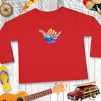 Red long-sleeve shirt with a colorful hand gesture design on a wooden surface with toys around.