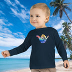 Child wearing a navy blue shirt with a colorful design on a beach with palm trees and blue sky.