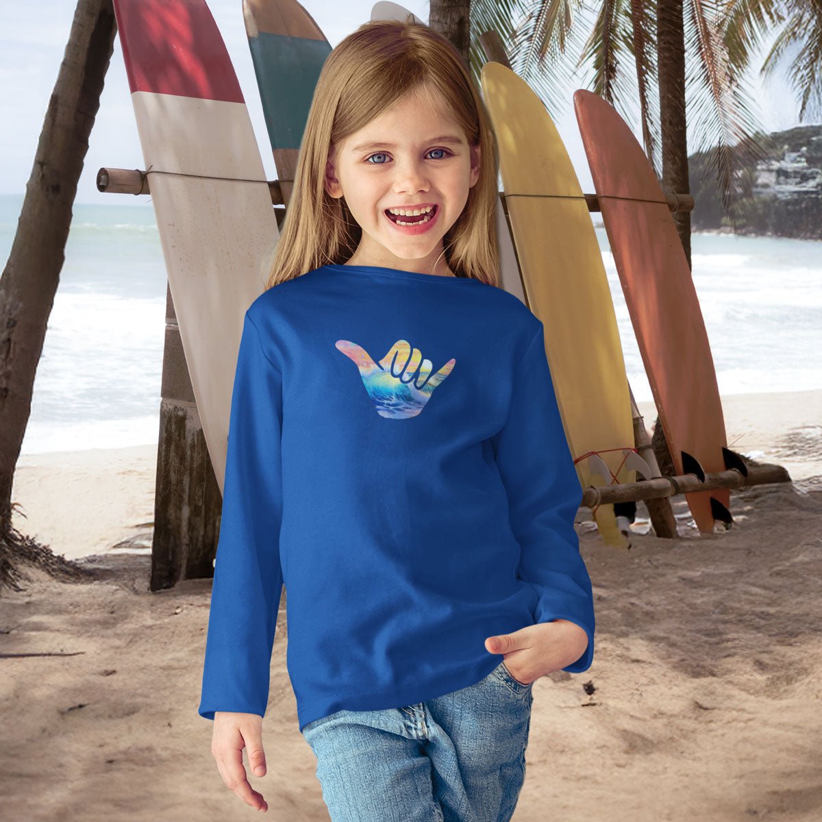 Child wearing a blue shirt with a colorful design on a beach with surfboards in the background