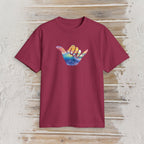 A short-sleeve crewneck t-shirt in maroon, featuring a colorful graphic of a hand sign with a sunset and ocean design, displayed flat against a rustic light wood background.