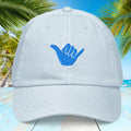 Light pastel blue cap with blue 'shaka' hand symbol on a tropical background