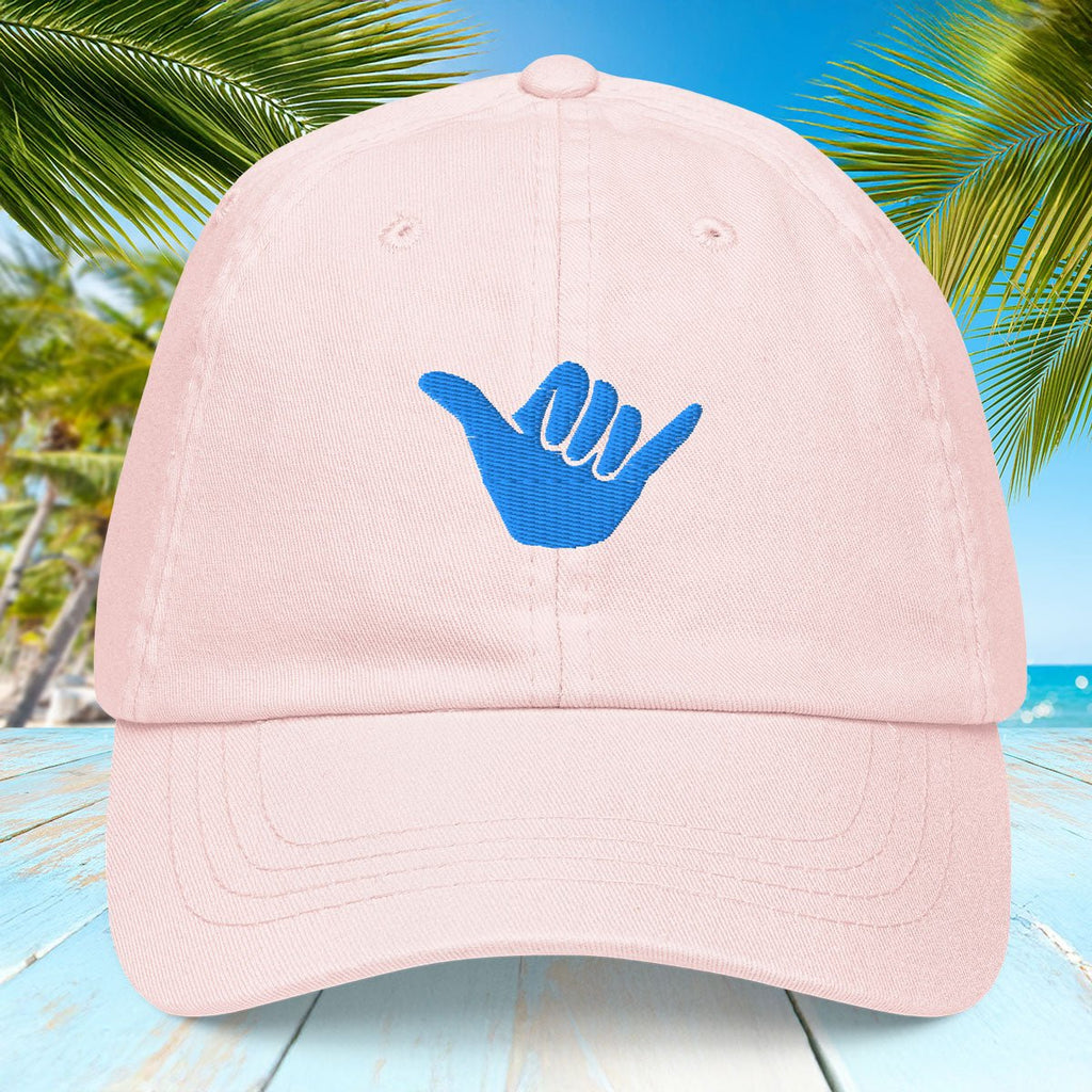 Pastel Pink cap with blue Shaka symbol against a tropical background