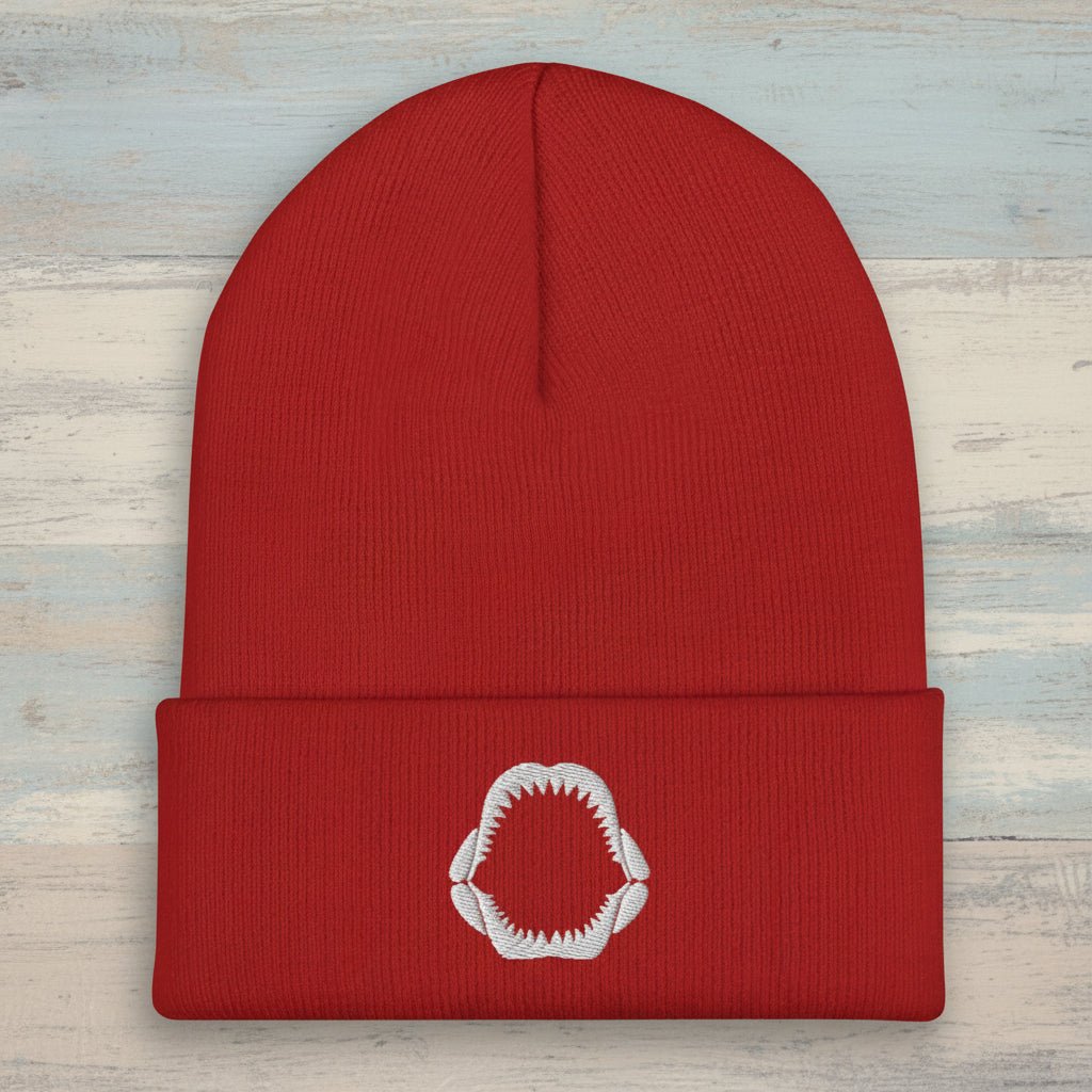 Black beanie with a white shark jaws embroidery on a rustic wood background