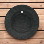 Underside of a black bucket hat with a subtle shark pattern lying on a rustic wood deck.