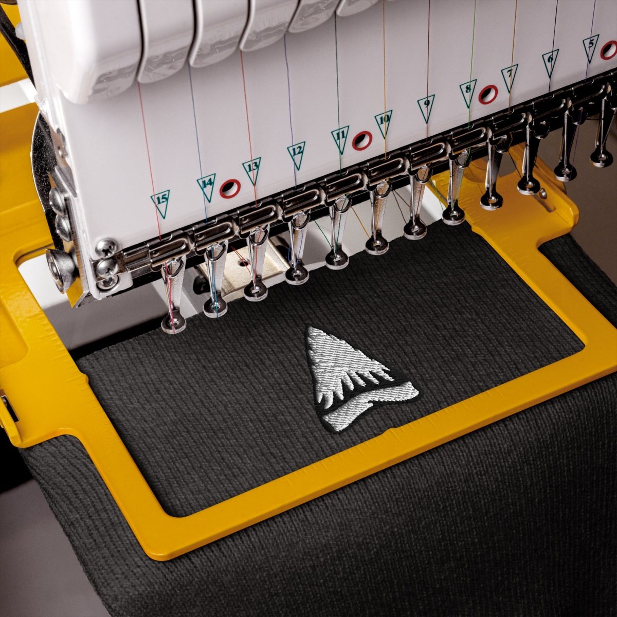 Close-up of an embroidery machine stitching a black fabric piece with a silver embroidered pine tree design.
