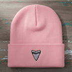 A light pink ribbed knit beanie hat with a folded cuff, featuring a small embroidered shark tooth graphic in black and white on the front center.