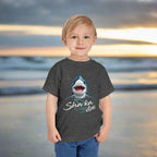 Child wearing a dark gray t-shirt with a shark graphic and 'Sharka Life' text standing on Daytona Beach