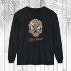 A black long-sleeve t-shirt with a colorful skull graphic made of various small objects and the text 'Shell-Raiser' in orange cursive, displayed on a white wood plank background.