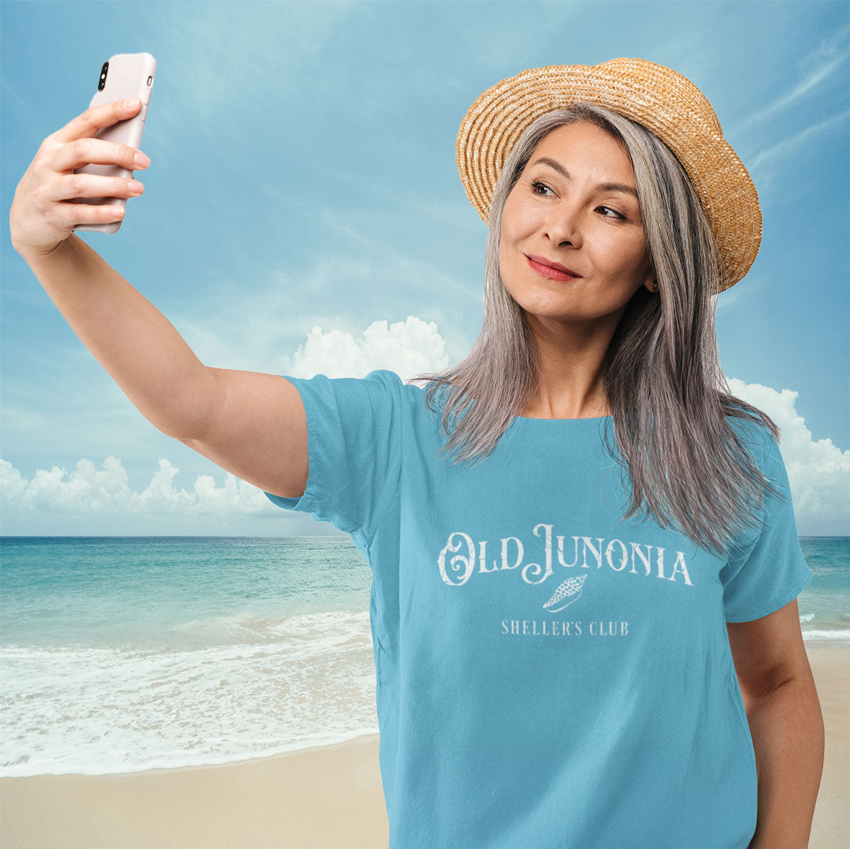 Woman taking a selfie on a beach wearing a blue t-shirt with 'Old Junonia' text.