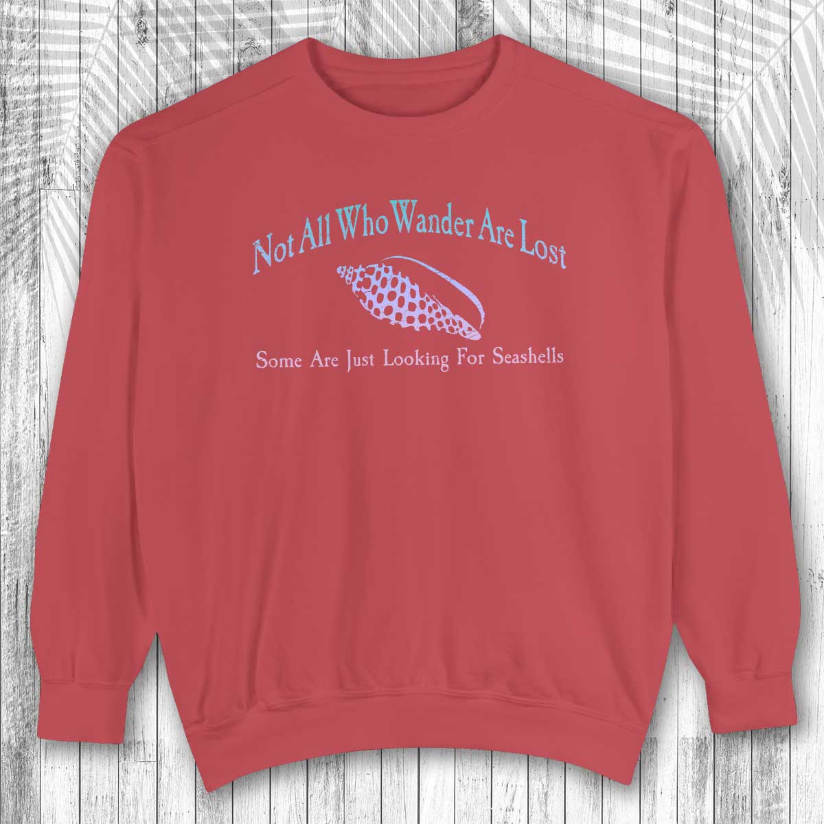 Red sweatshirt with text and a seashell graphic on a wooden surface