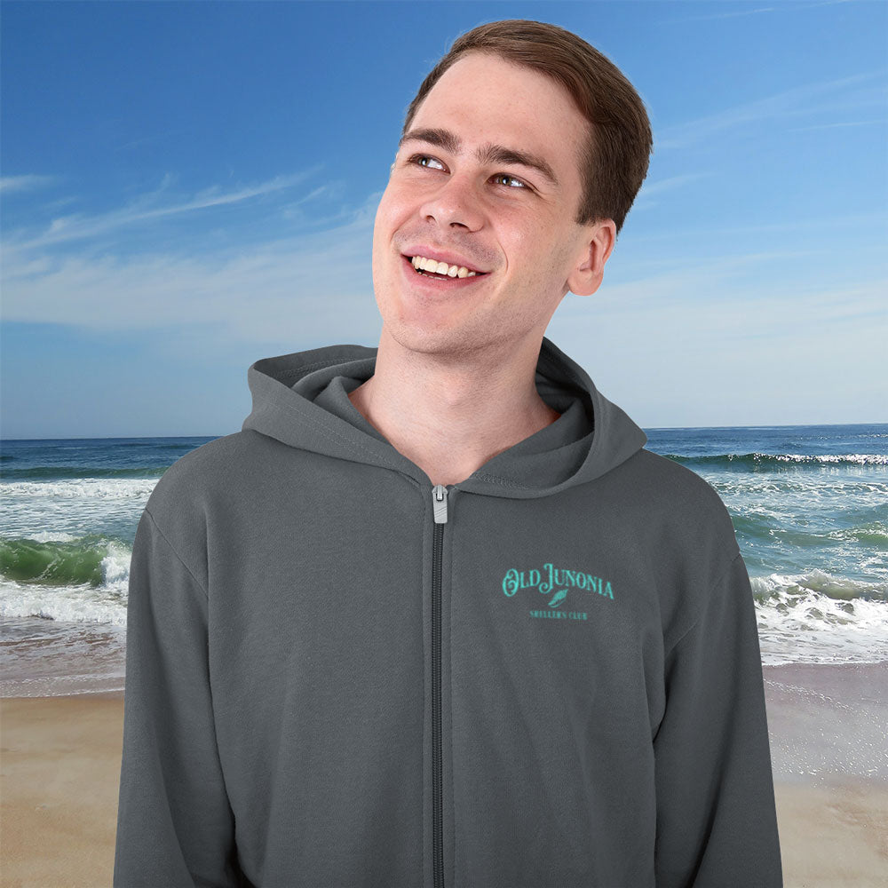 Person wearing a gray hoodie with a brand logo on a beach