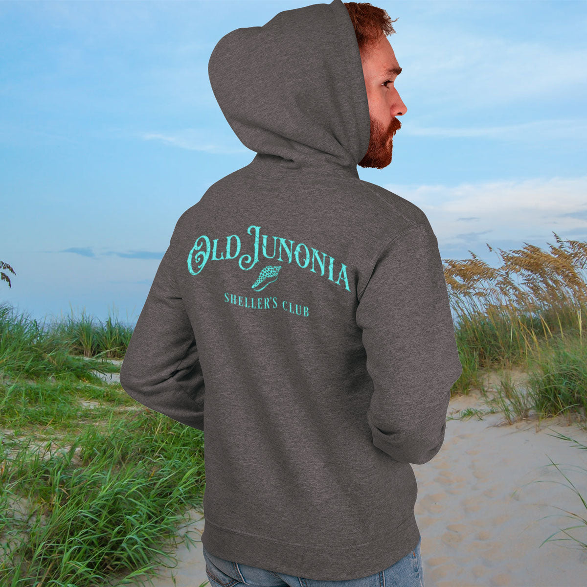 Person wearing a gray hoodie with 'Old Junonia' text on a beach
