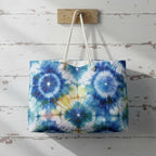 Tie-dye patterned bag with white handles hanging on a wooden hook against a rustic wooden wall.
