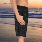 Surfer Dude wearing cool black board shorts with a shark pattern by Bongo Beachwear standing on the beach