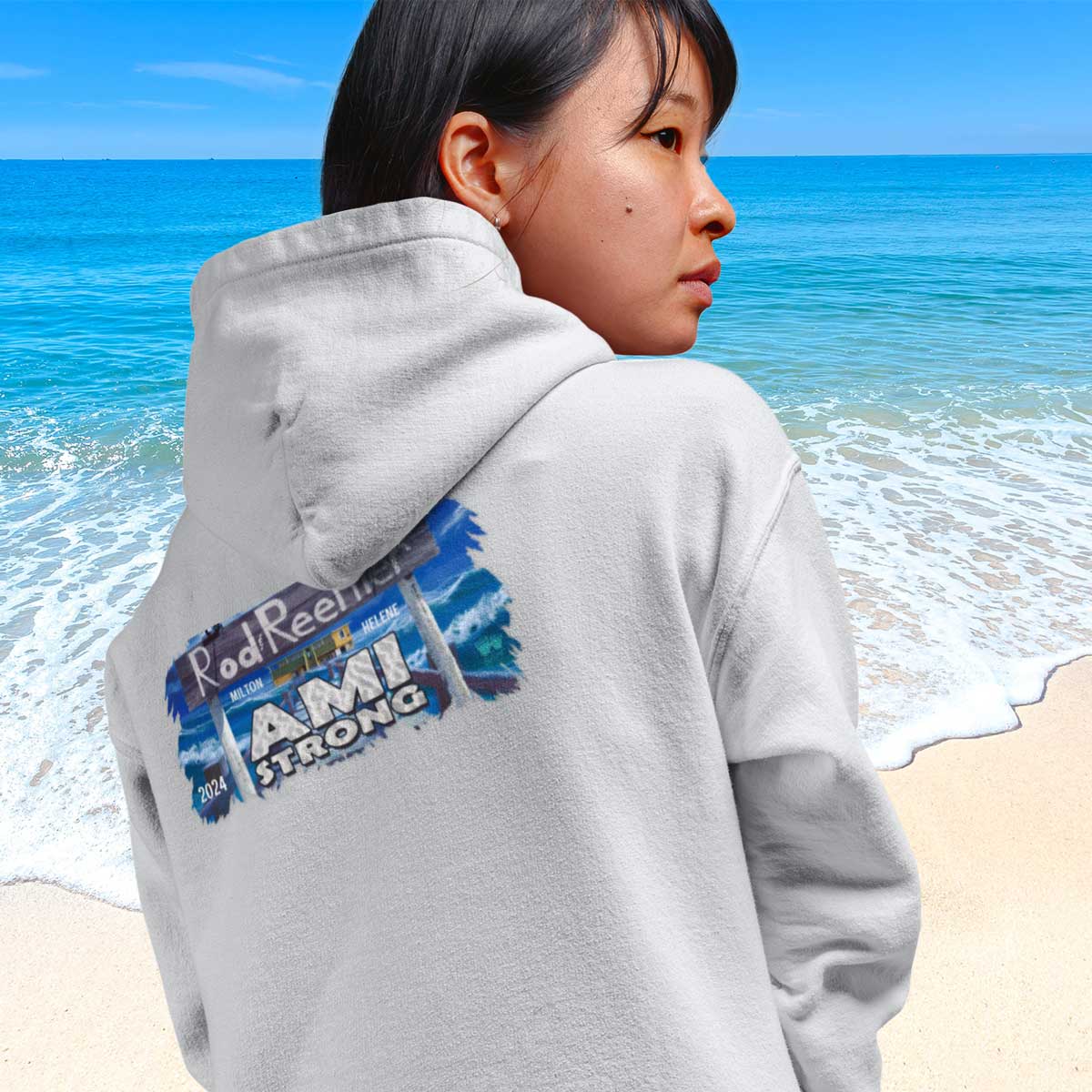 Person wearing a gray hoodie with fundraiser art and 'AMI STRONG' text on the beach