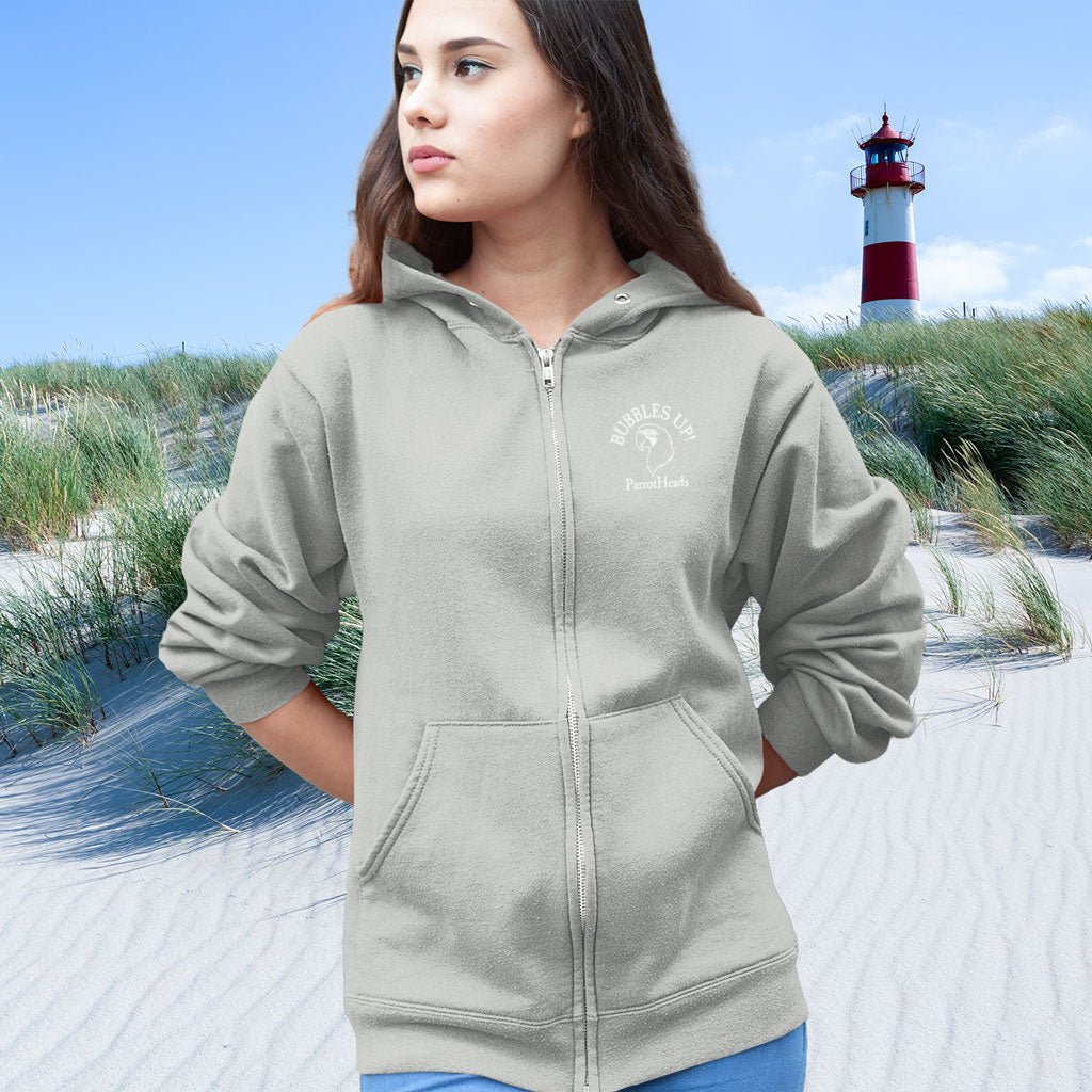 Woman wearing a gray ParrotHead Hoodie with a logo on a beach with a lighthouse in the background