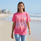 Woman wearing a pink t-shirt with a colorful American flag design on a beach.