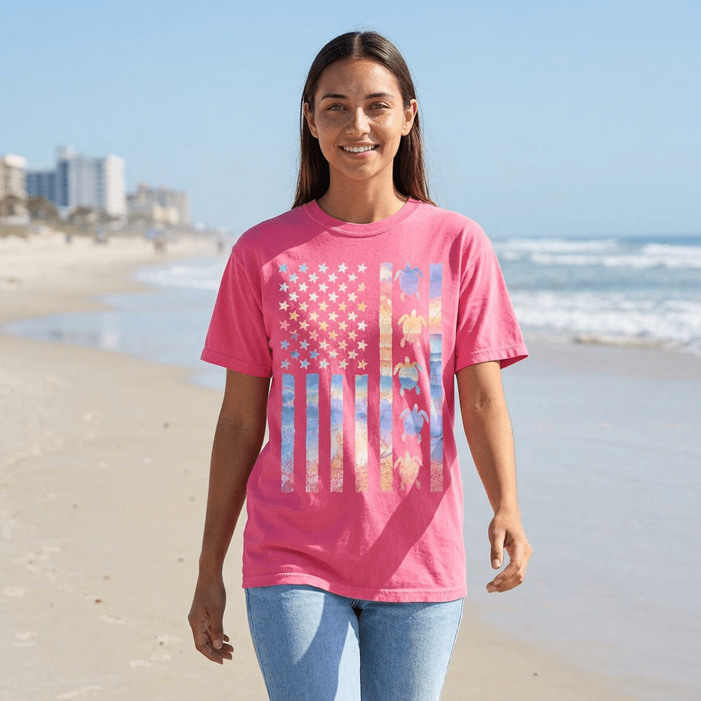 Woman wearing a pink t-shirt with a colorful American flag design on a beach.