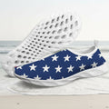A pair of slip-on water shoes with a navy blue and white star pattern, featuring a white textured sole, shown against a faded beach background.