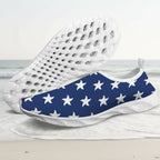 A pair of slip-on water shoes with a navy blue and white star pattern, featuring a white textured sole, shown against a faded beach background.