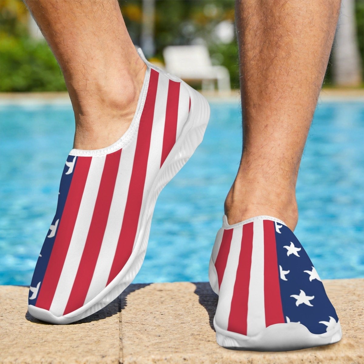 A person wearing slip-on water shoes with an American flag print, standing on a pool deck with a swimming pool in the background.