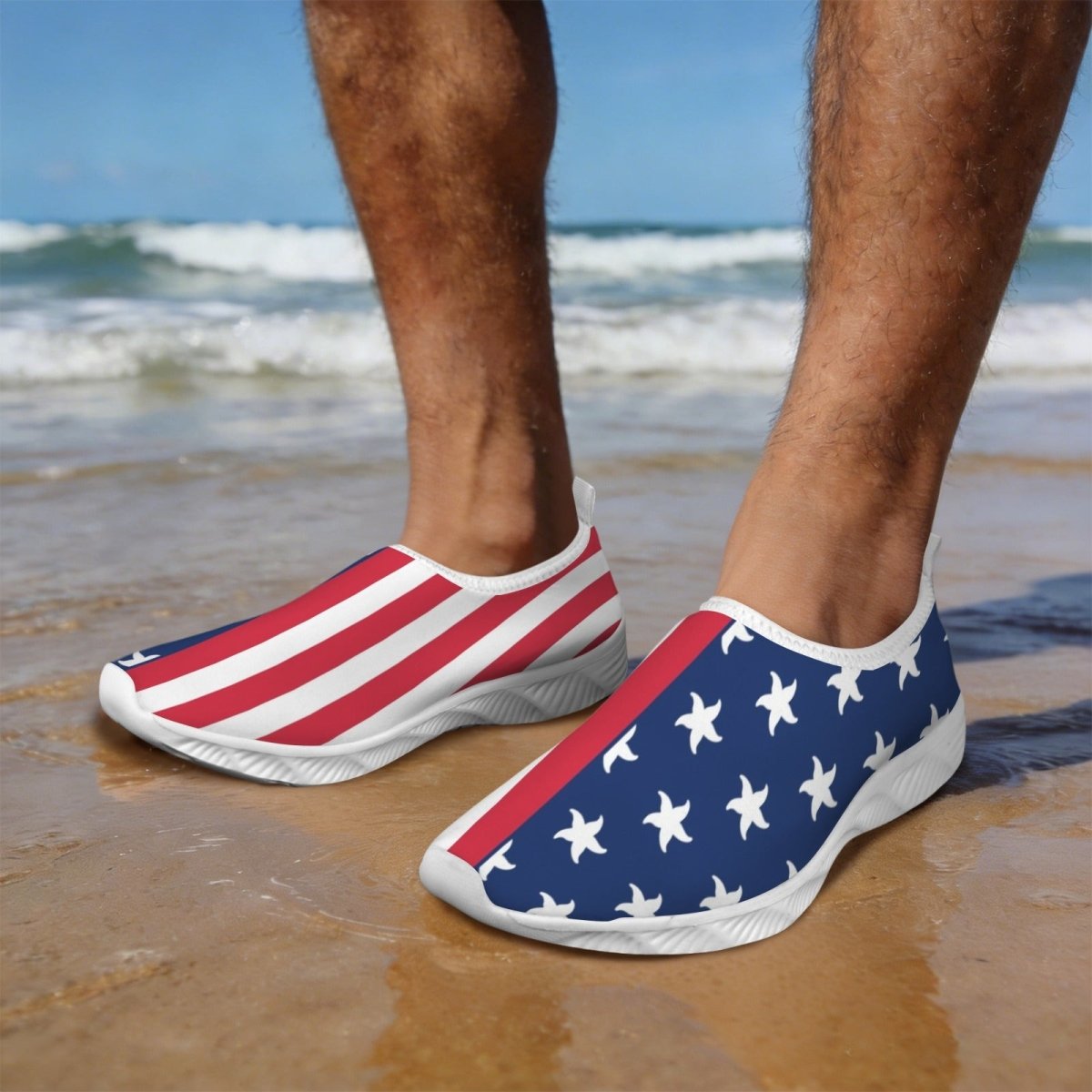 A person standing on a beach wearing Beach Sneakers with an American flag design, one shoe showing red and white stripes and the other showing white stars on a blue background.