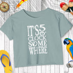 Light blue t-shirt with 'It's 5 o'clock somewhere' text on a wooden surface with decorative items.