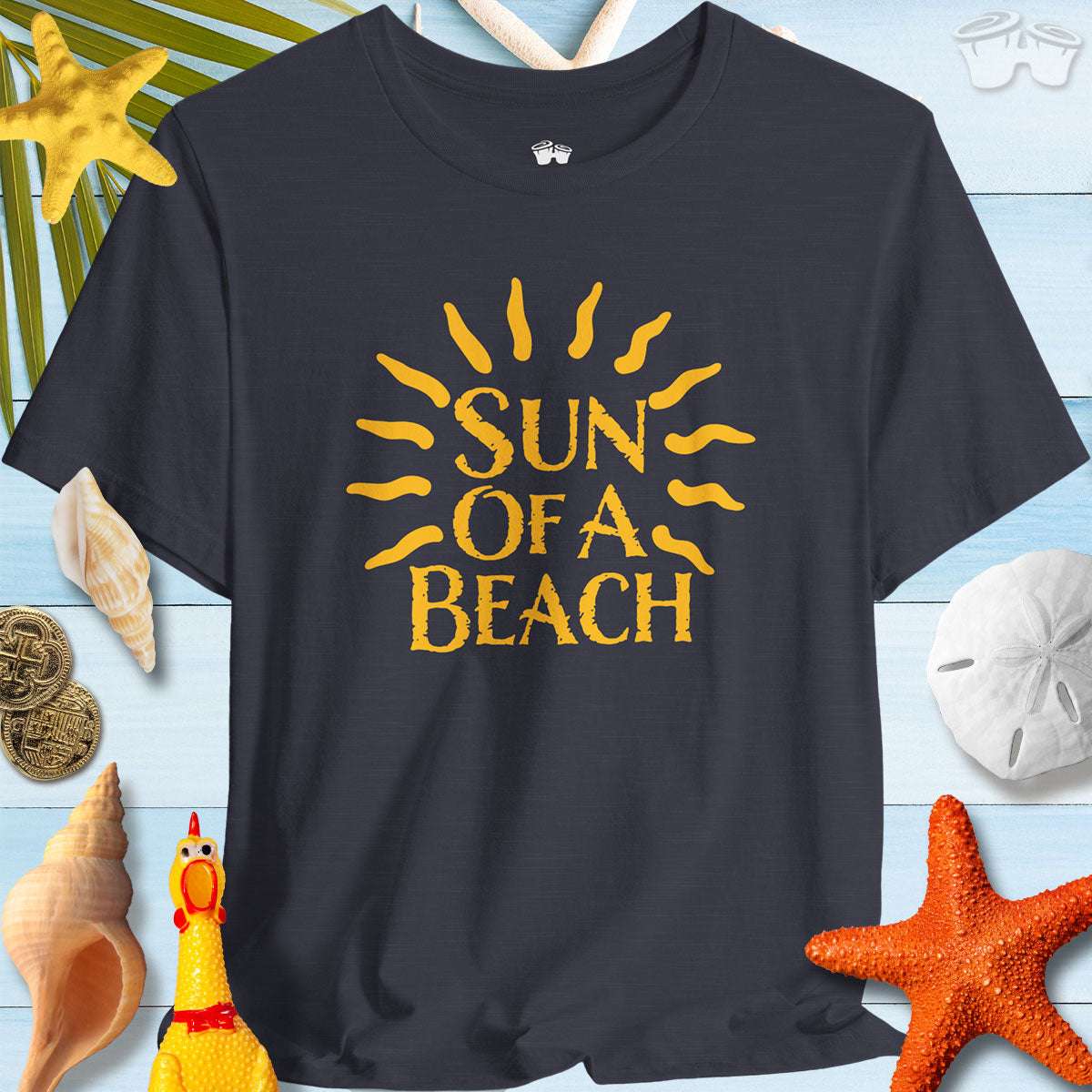 Sun Of A Beach Bella Canvas Tee shirt on a beach-themed background with seashells and a starfish.