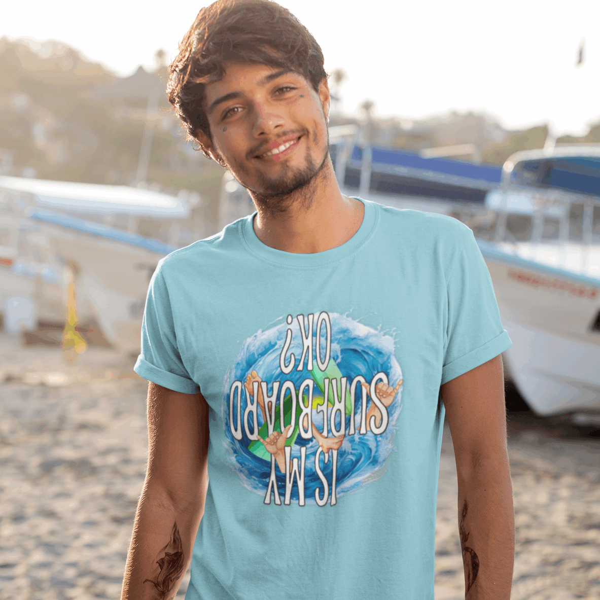 Surfer dude standing in sand next to some boats wearing a Bongo Beachwear funny serfer's tee.
