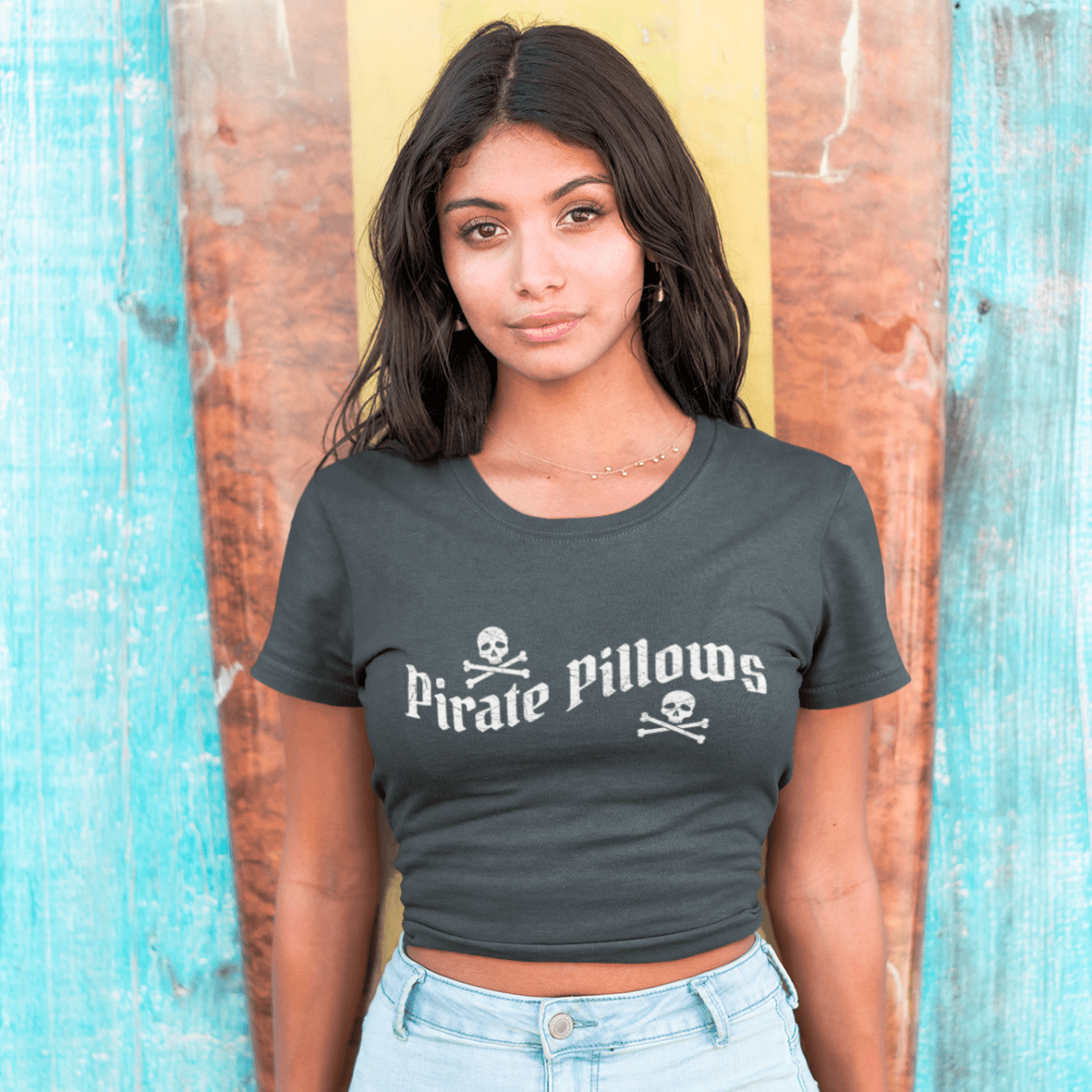 Woman wearing a dark gray t-shirt with 'Pirate Pillows' text and skull design, standing against a wooden background.
