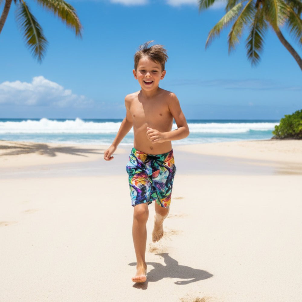 Child wearing Surfer Kids Board Shorts running on a sandy beach with palm trees and ocean in the background