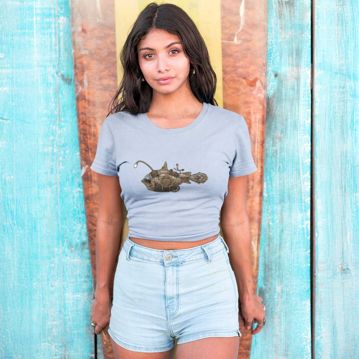 Woman wearing a light blue t-shirt with a graphic design in front of a wooden wall.