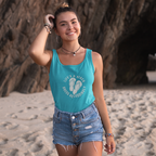 Woman in sapphire tank top and denim shorts standing on a beach with rocky background