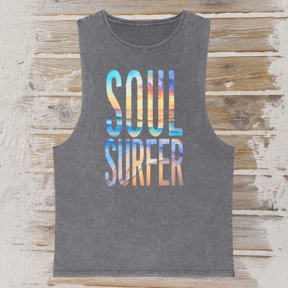 A dark gray sleeveless tank top with 'SOUL SURFER' printed in a colorful gradient wave pattern, displayed flat on a rustic wooden plank background.