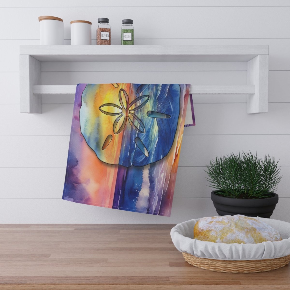 Colorful towel with a floral design hanging on a white wall above a wooden surface with a basket and plant.