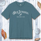 Teal t-shirt with 'Old Junonia Sheller's Club' text on a wooden surface with shells.