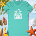 Women's Salty Beach Mom turquoise tee on beach-themed background with seashells and starfish.
