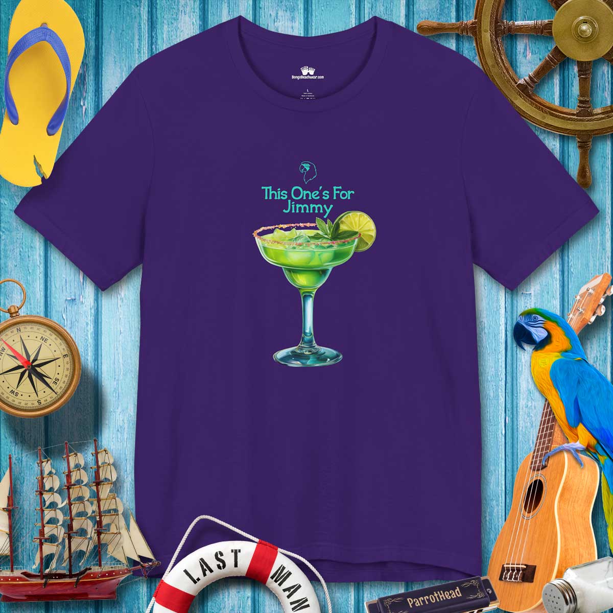 Purple t-shirt with a cocktail graphic and text on a blue wooden background with tropical items.