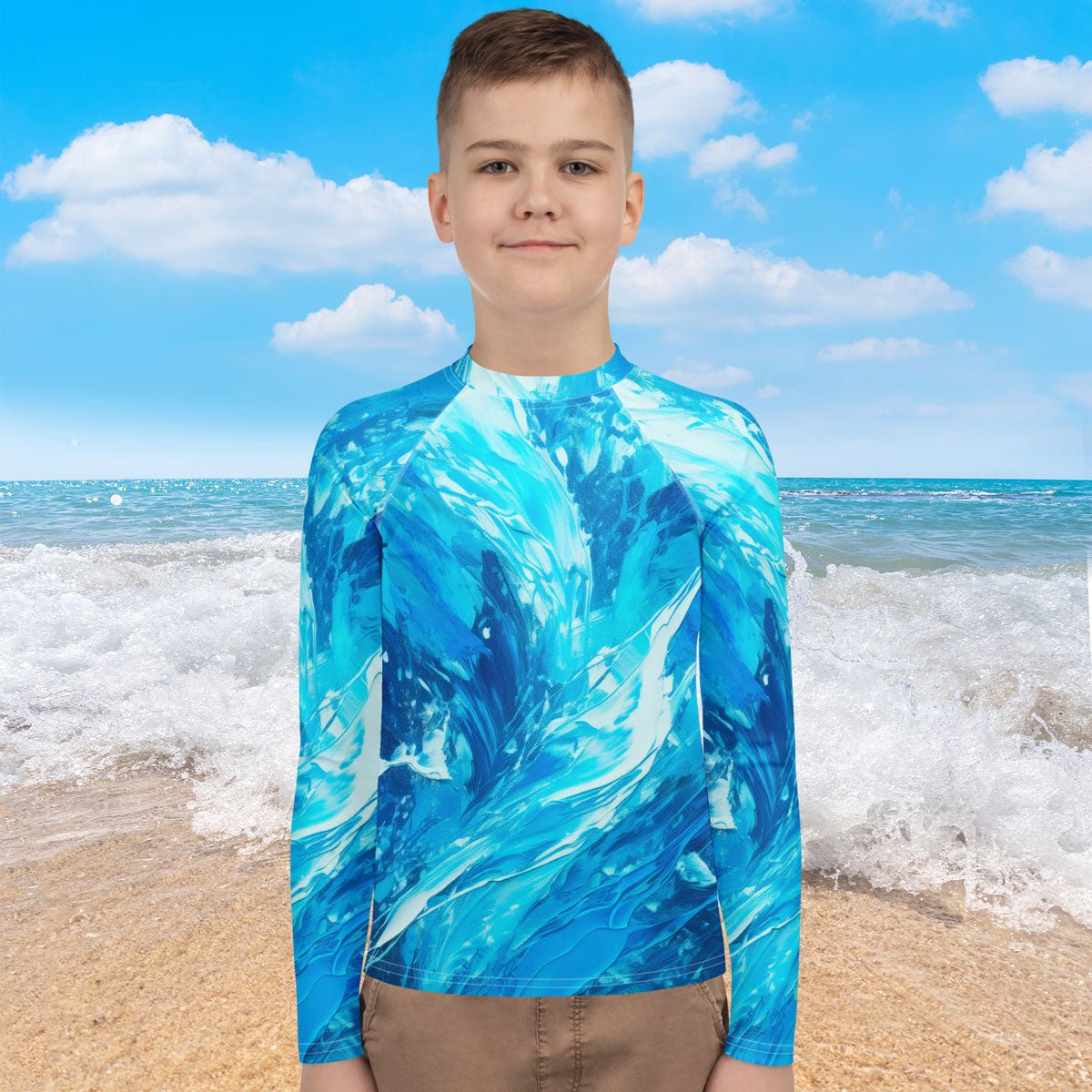 Teen wearing a blue wave patterned rash guard on a beach with ocean and sky in the background