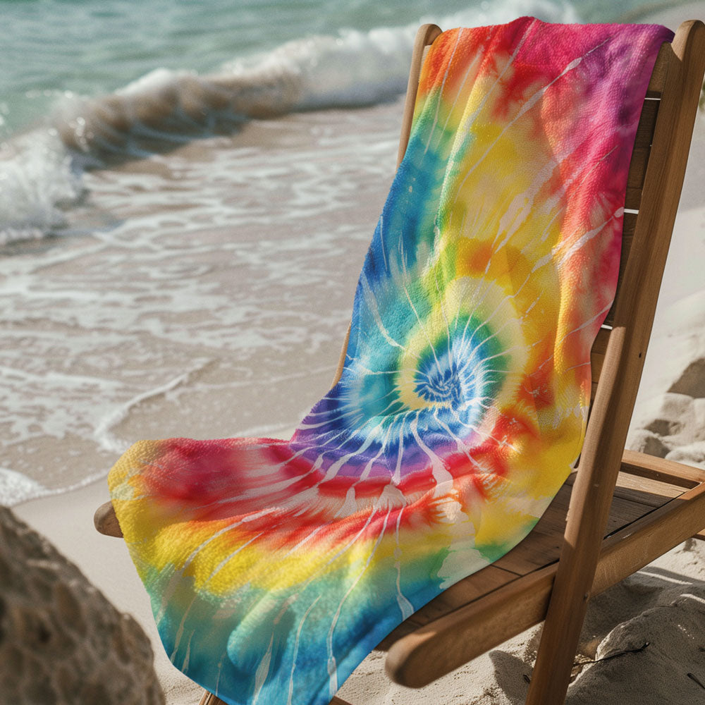 Deck chair next to the ocean draped with a cool tie-dye beach towel.