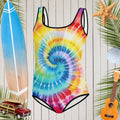 Classic Spiral Tie Dye in Cool Vibrant colors on Girls One Piece Swimsuit in front of a rustic nautical wall with surf icons all around
