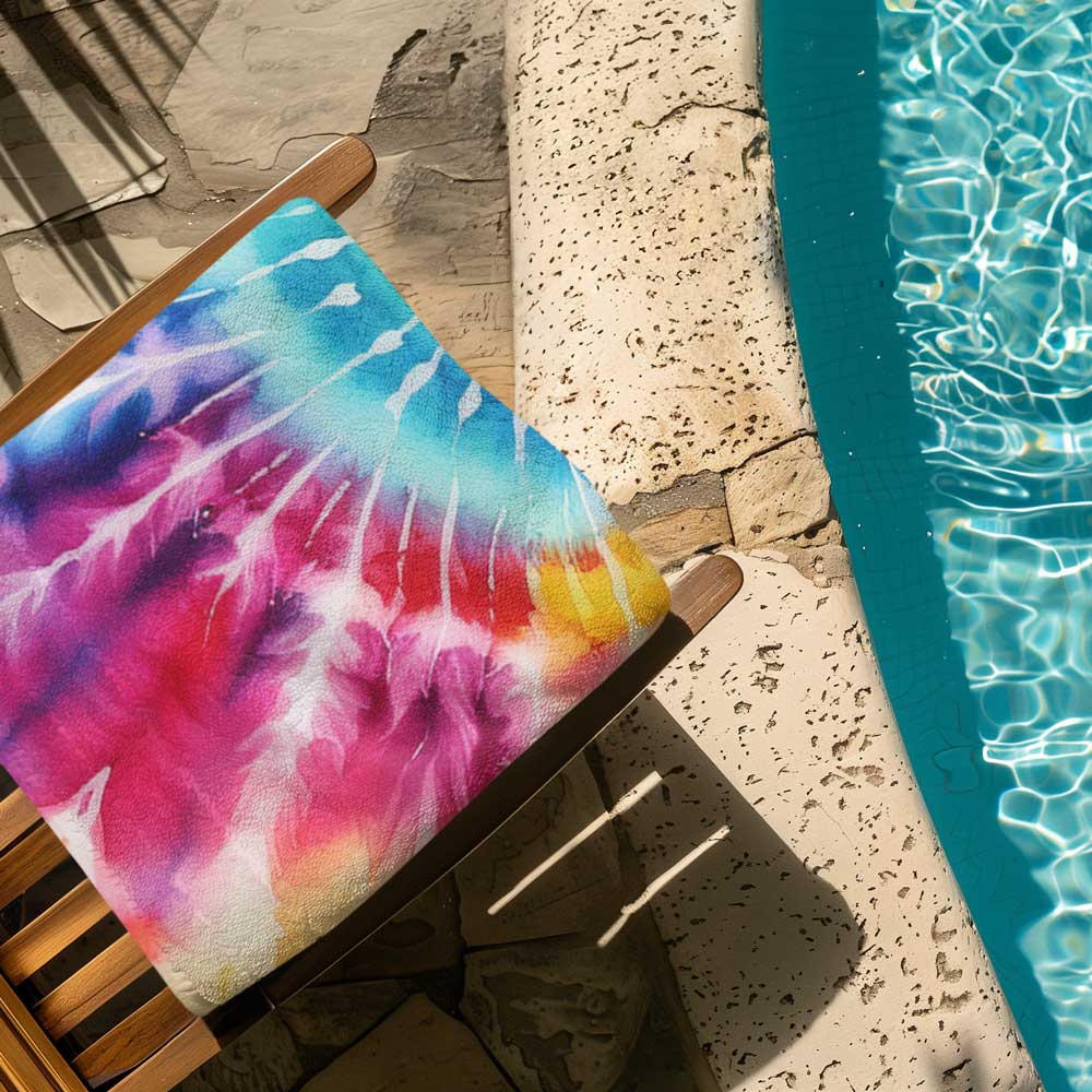 Folded Tie-Dye beach towel on a poolside deck chair.