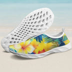 A pair of slip-on water shoes with a white sole and a tropical floral print on the upper. One shoe is shown from the side displaying a yellow hibiscus flower and palm leaves, while the other is turned to show the textured white sole.