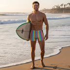 Man in colorful swim shorts holding a surfboard on a beach
